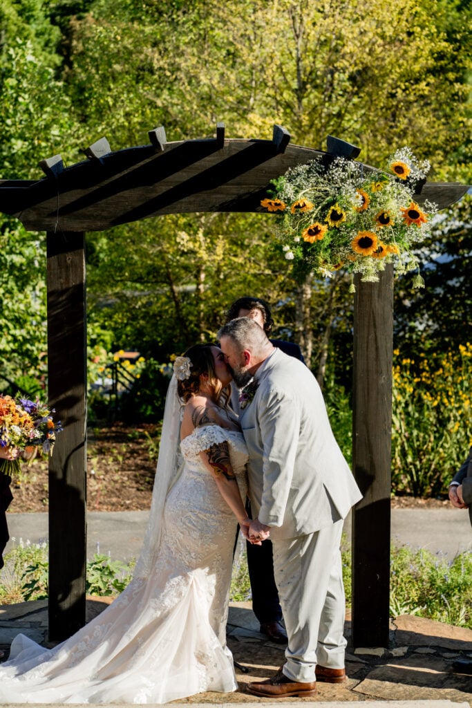 Sun Flower Hill Farm bride groom kiss under wooden pergola sunflowers